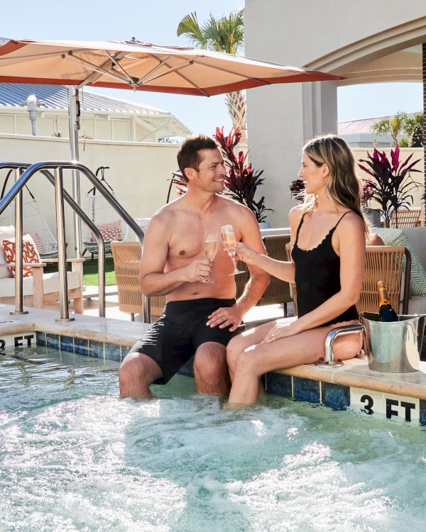 People are enjoying a spa day, sitting by a pool, sipping champagne, and relaxing in robes.