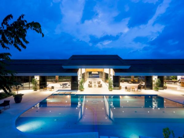 A modern building with an illuminated outdoor pool at night, surrounded by seating areas, under a deep blue sky.