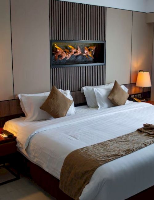 A hotel room with a large bed, decorative pillows, side lamps, and a wall art piece above the bed, near a window covered with curtains.