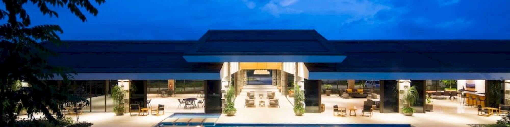 A luxurious pool area is illuminated at night, with a modern building in the background and a clear, tranquil sky above.