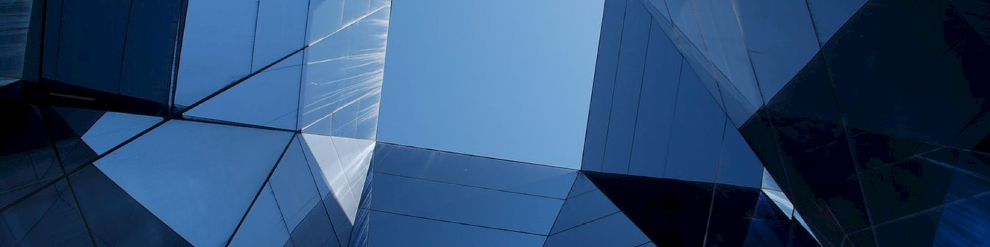 The image shows a geometric pattern formed by modern glass buildings, reflecting the sky and each other at various angles.