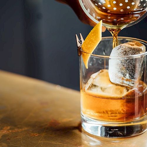 A cocktail is being poured into a glass with ice and a twist of citrus peel.