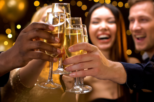 A group of people celebrating with champagne flutes, festive lights in the background, and cheerful expressions.