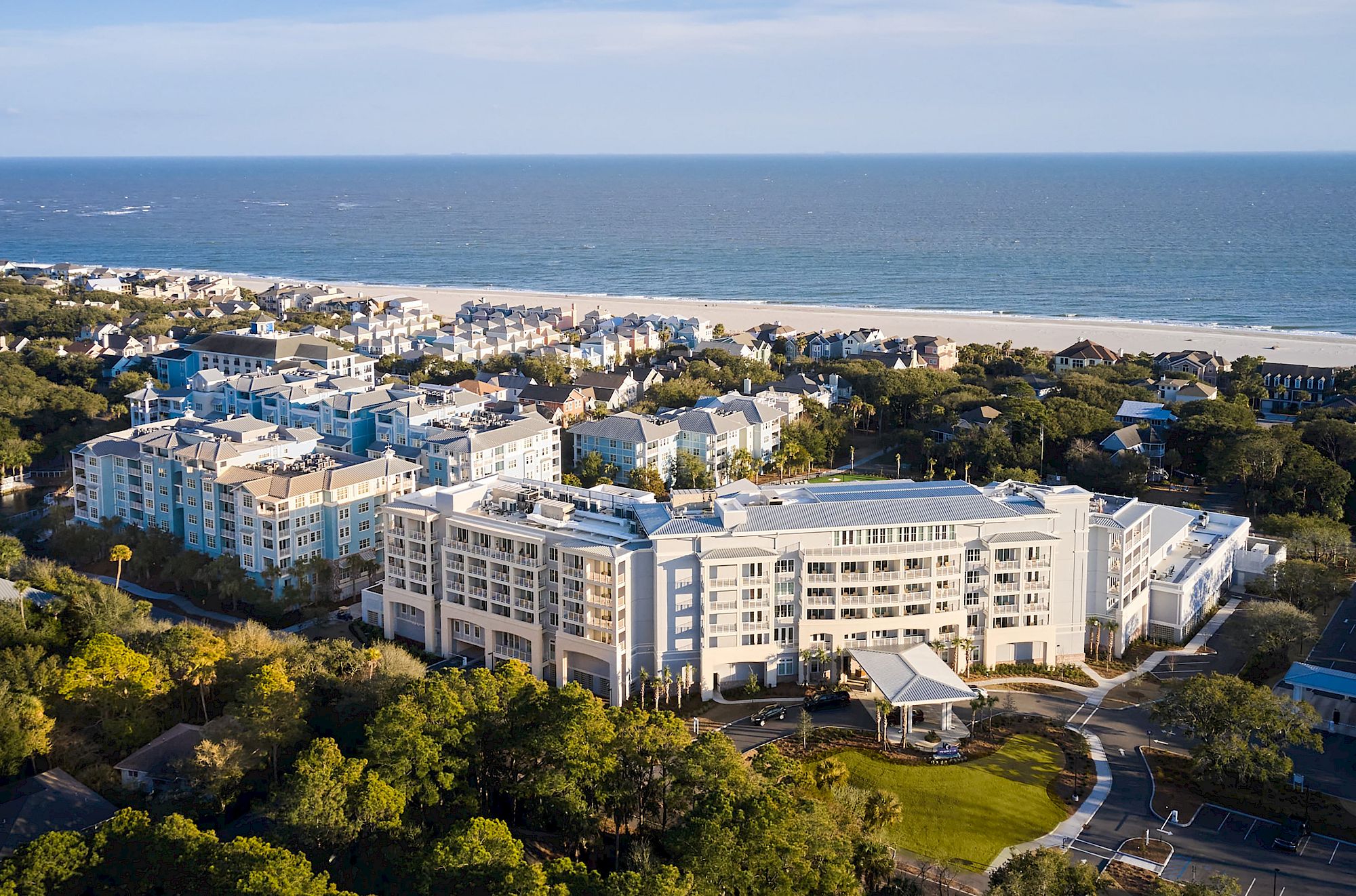Aerial view of a beachfront resort with multiple buildings surrounded by greenery and a sandy beach next to the ocean.