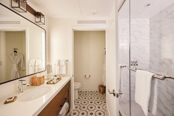 A modern bathroom with a sink, large mirror, wooden cabinet, towels, shower with glass door, and patterned floor tiles in neutral tones.