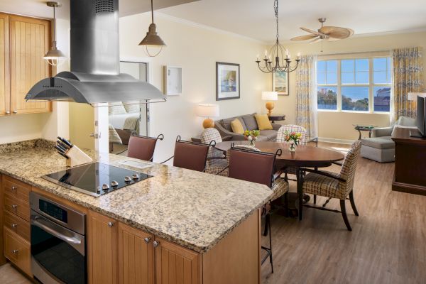 The image shows a modern kitchen and living area with a stove, granite countertops, dining table, sofa, armchairs, and large windows.
