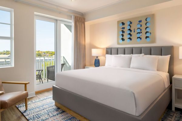 A cozy bedroom features a king-size bed, two lamps, an armchair, and a balcony with a view. There's a decorative piece above the bed.