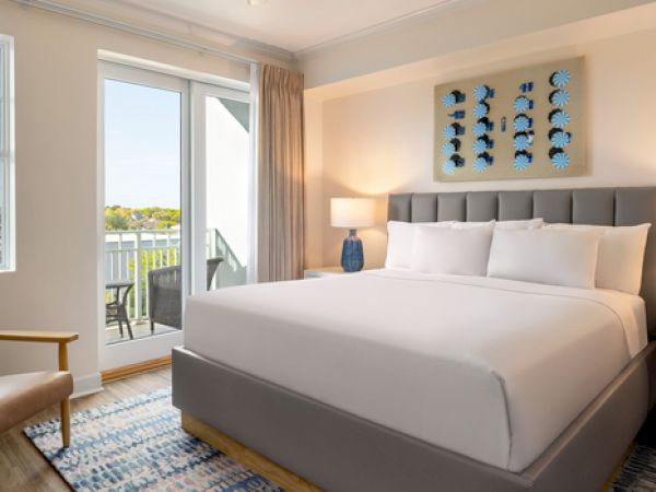 A cozy bedroom features a king-size bed, two lamps, an armchair, and a balcony with a view. There's a decorative piece above the bed.