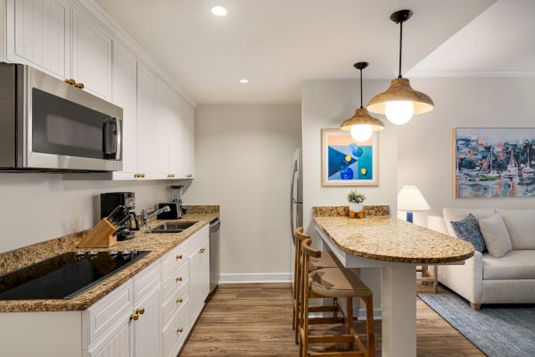 A modern kitchen with white cabinets, stainless steel appliances, and a granite countertop bar with pendant lights and wooden stools.