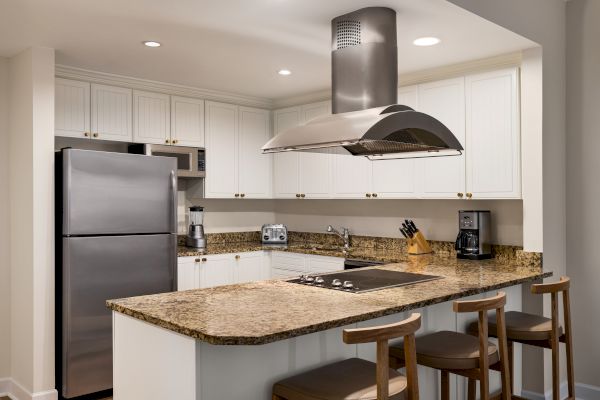 A modern kitchen with granite countertops, stainless steel appliances, white cabinets, and a central island with bar stools.