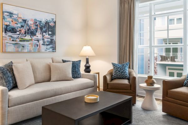 A modern living room with a sofa, two armchairs, a coffee table, lamps, abstract artwork, and large windows with a view.