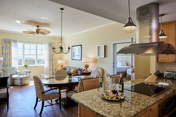 A cozy living area with a dining table, chairs, and a kitchen counter with snacks and wine; a bedroom is visible through a doorway.