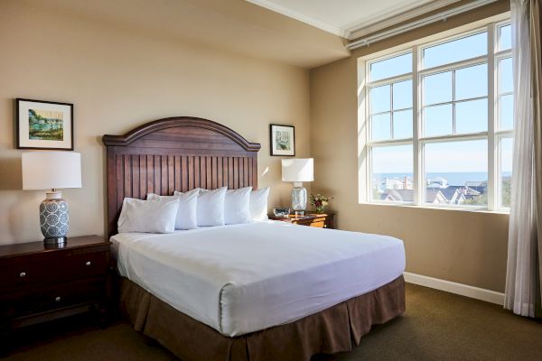 A cozy bedroom with a wooden bed, white linens, bedside tables, lamps, and large windows showing a scenic outdoor view ends the sentence.