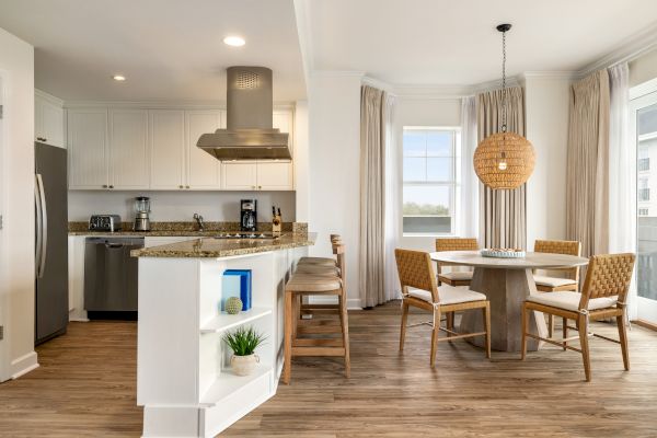A modern kitchen-dining area with granite countertops, a round table, wicker chairs, and a woven pendant light; bright and inviting space.