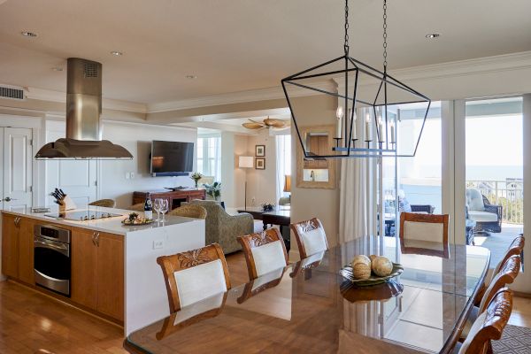 A modern open-plan living area with kitchen and dining, featuring elegant lighting, a TV, and patio view through large glass doors.