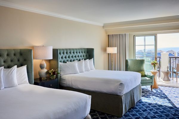 A cozy hotel room with two beds, a chair, and a balcony view of the sea, featuring elegant decor and soft lighting.