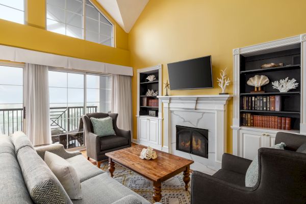 A cozy living room with yellow walls, gray sofas, a wooden table, fireplace, and large TV, featuring a high ceiling and tall windows.