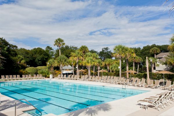 A swimming pool surrounded by lounge chairs and palm trees under a partly cloudy sky.