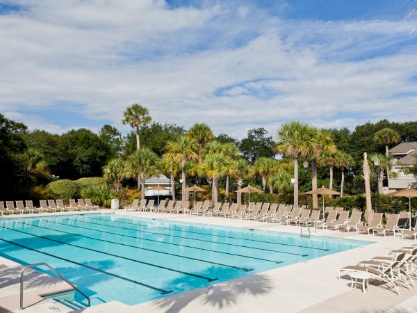 A swimming pool surrounded by lounge chairs and palm trees under a partly cloudy sky.