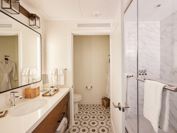 A modern bathroom with a double sink, large mirror, hanging robes, and glass-enclosed shower with marble tiles.