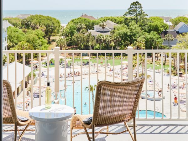 Two wicker chairs and a table with wine overlook a pool and trees, with the ocean in the background.