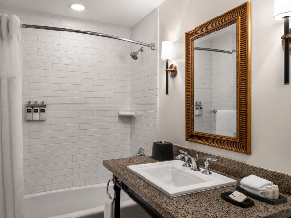 A modern bathroom with a bathtub, white tiles, a mirror, and a sink on a granite countertop.