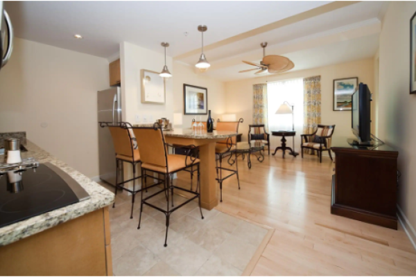 A modern kitchen and dining area with granite countertops, bar stools, a dining table, and a living space with a TV and chairs.