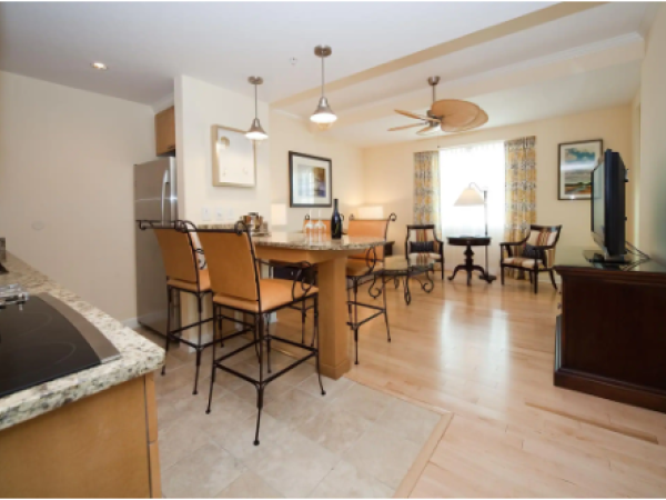 A modern kitchen and dining area with granite countertops, bar stools, a dining table, and a living space with a TV and chairs.