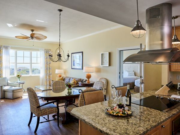 A cozy living area with a dining table, chairs, and a kitchen counter with snacks and wine; a bedroom is visible through a doorway.