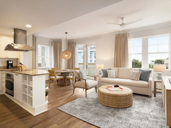 A modern open-plan living area with a kitchen, dining set, sofa, TV, and decor, featuring light colors and wood flooring.