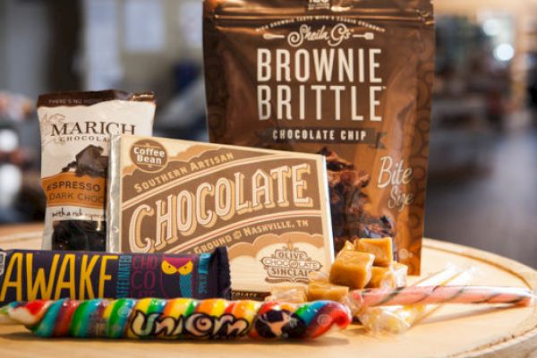 The image shows various sweet treats, including Brownie Brittle, chocolate, candy sticks, and lollipops, all displayed on a wooden surface.