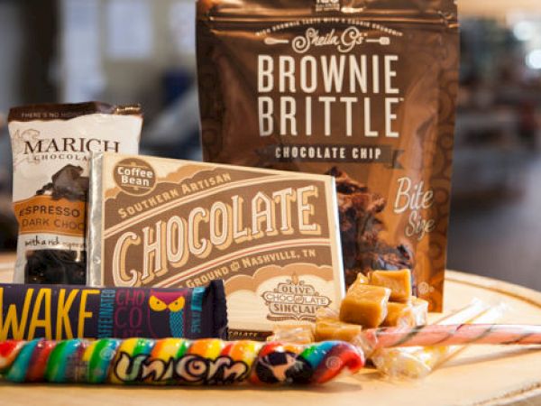 The image shows various sweet treats, including Brownie Brittle, chocolate, candy sticks, and lollipops, all displayed on a wooden surface.