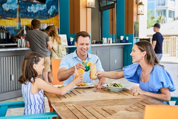 A family is enjoying a meal together at an outdoor restaurant, toasting with colorful drinks.