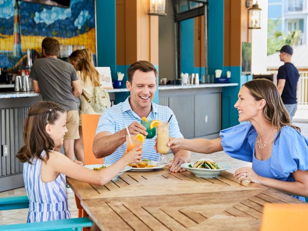 A family is enjoying a meal together at an outdoor restaurant, toasting with colorful drinks.