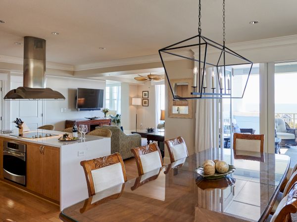 A modern open-plan living area with kitchen and dining, featuring elegant lighting, a TV, and patio view through large glass doors.