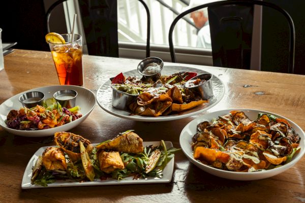 A table with various dishes: skewers, roasted vegetables, and a drink by a window.