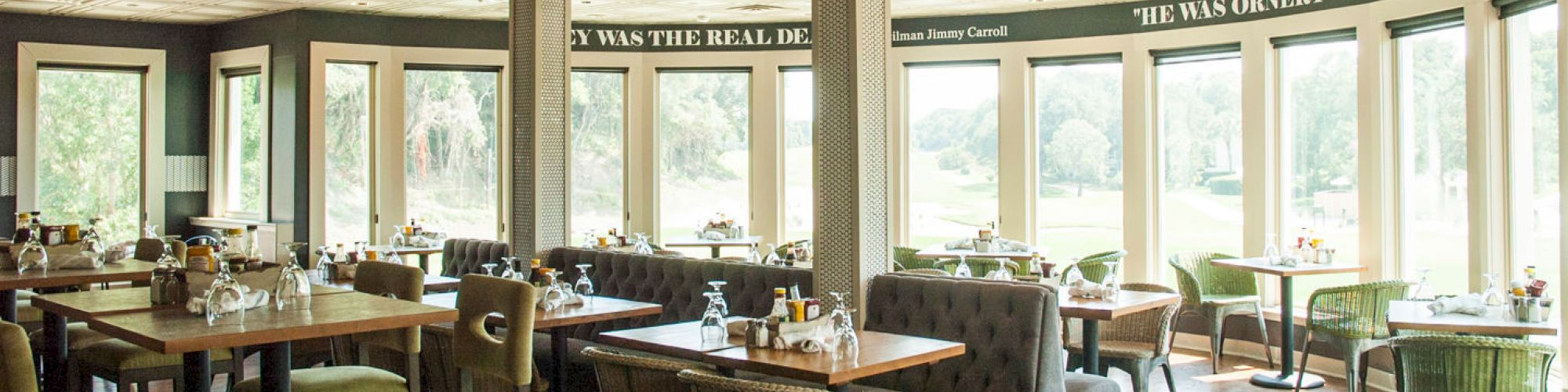 A bright, modern restaurant with wooden tables, green chairs, large windows, and decorative text on the walls.