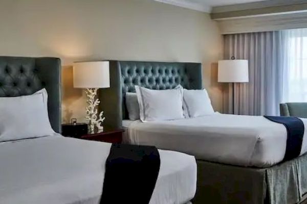 The image shows a hotel room with two large beds, white bedding, dark headboards, and lamps beside each bed.