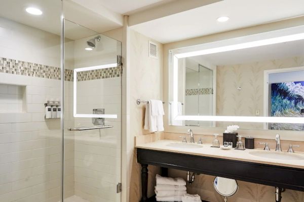 A modern bathroom with a glass shower, dual sinks, large mirror, and neatly arranged toiletries and towels.