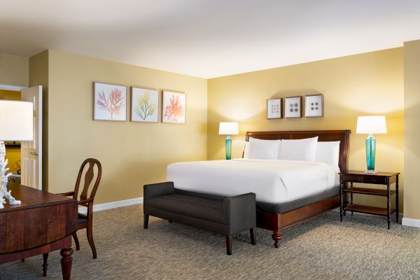A cozy bedroom with a large bed, bedside tables, lamps, and wall art; includes a desk and chair against a neutral-toned wall.