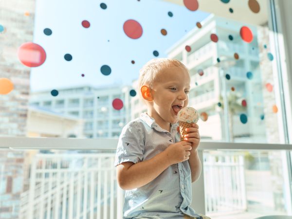 A happy child licking ice cream in a bright, festive setting with colorful balloons in the background.