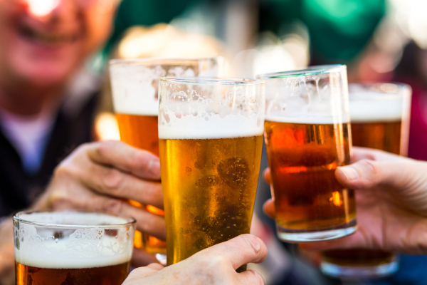 People are raising glasses of beer in a toast, suggesting a celebration or social gathering outdoors.