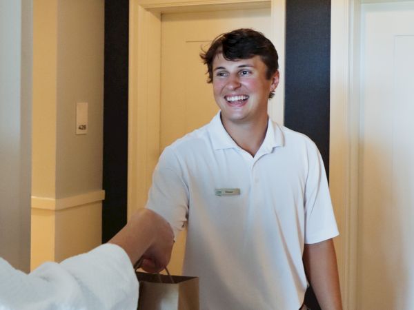 A person in a white shirt is smiling and receiving a bag from another person in a hallway.
