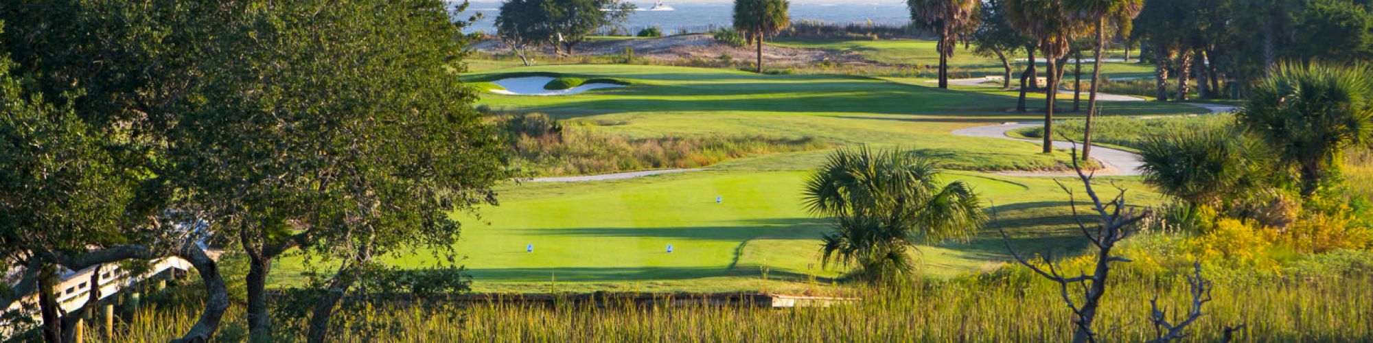 A lush golf course with neatly manicured greens, trees, and a view of water in the background.