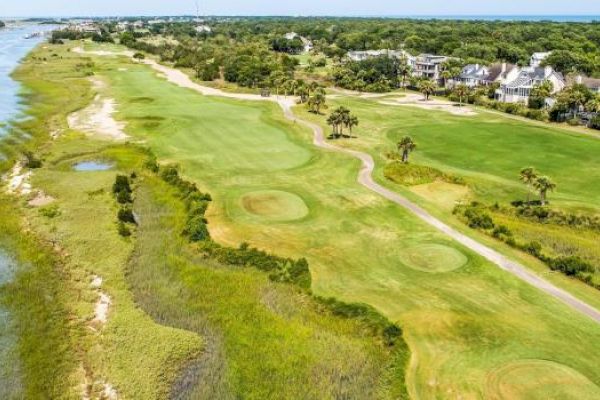 A coastal golf course with lush greenery, water channels, and houses in the distance.