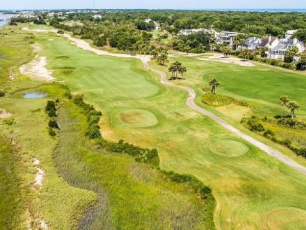 A coastal golf course with lush greenery, water channels, and houses in the distance.