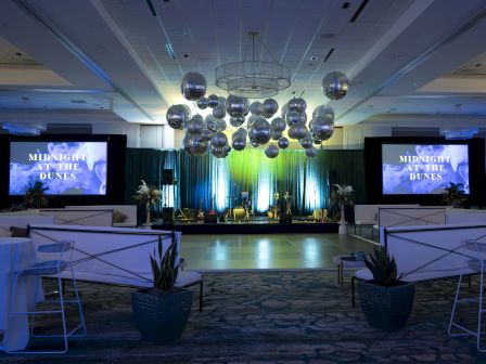 The image shows an event space with a stage, large screens, and decorative hanging spheres, titled "Midnight at the Dunes."