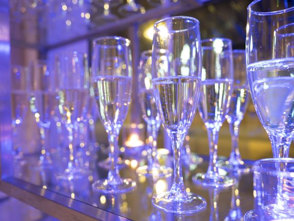 A row of empty champagne flutes on a reflective surface, illuminated by soft blue lighting.