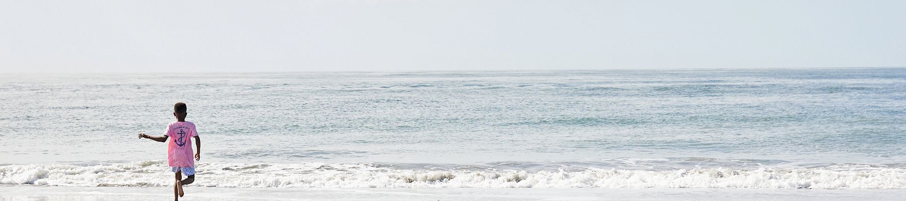 A person in a pink shirt runs toward the ocean on a sandy beach under a cloudy sky.