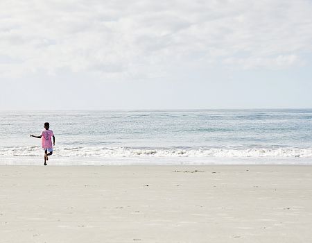 A person in a pink shirt runs toward the ocean on a sandy beach under a cloudy sky.
